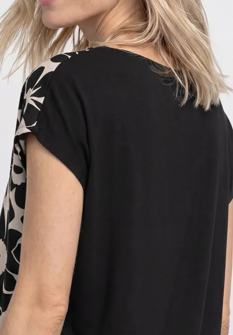 Rückenansicht einer Frau in einem schwarzen Shirt mit beigen, abstrakten Mustern an den Ärmeln.