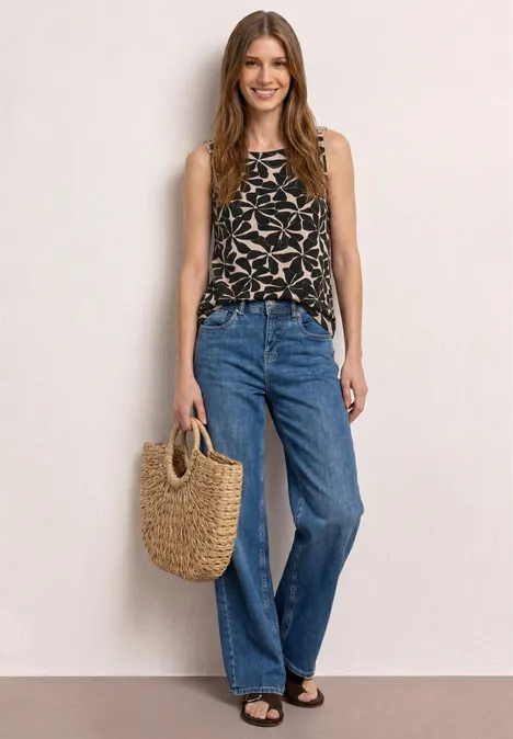Top met ronde hals en schouderdetails Black Vrouw in wijde spijkerbroek, top met print en een gevlochten strooien tas.