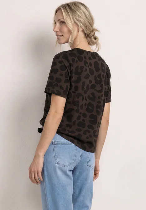 Vrouw van achteren in een lichtblauwe spijkerbroek en een bruin leopardprint t-shirt voor een neutrale achtergrond.