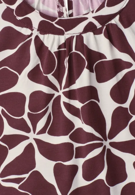 Close-up van een bordeaux T-shirt met witte bloemprint in organische vormen.
