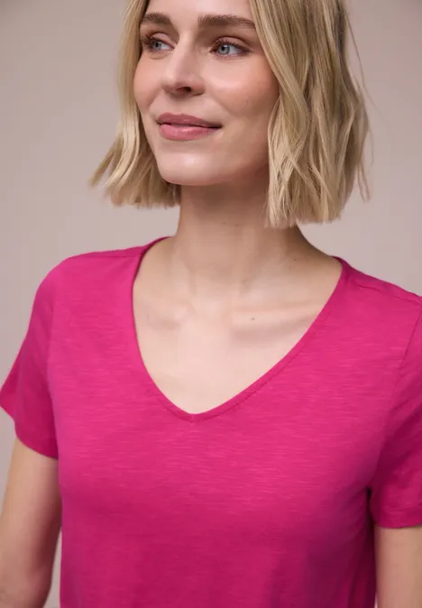 Een persoon draagt een roze t-shirt voor een lichte, neutrale achtergrond.