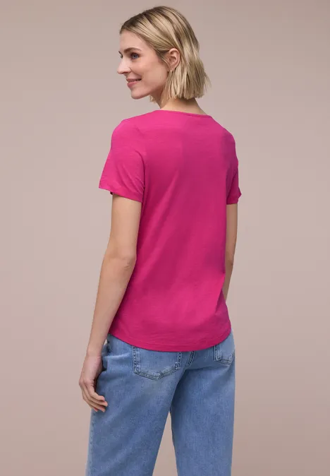 Vrouw van achter gezien in een roze t-shirt en blauwe spijkerbroek voor neutrale achtergrond.