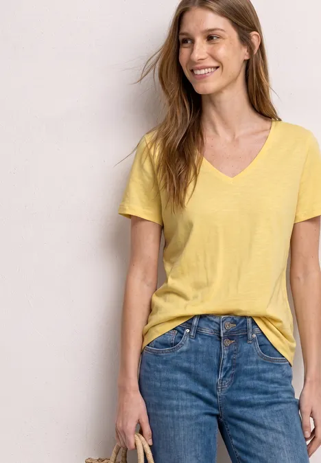Femme en t-shirt jaune à col en V et jean bleu, tenant un sac à main sur le côté.