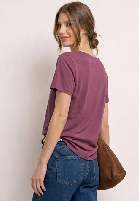 Vrouw van achteren met paars T-shirt, spijkerbroek en bruine schoudertas.