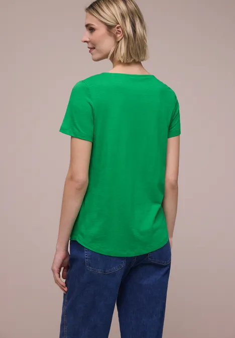 Vrouw met kort blond haar in een groen T-shirt, rugaanzicht tegen neutrale achtergrond.