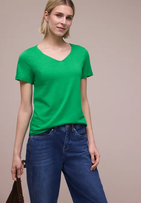 Vrouw met groen T-shirt en blauwe jeans, houdt een handtas vast.
