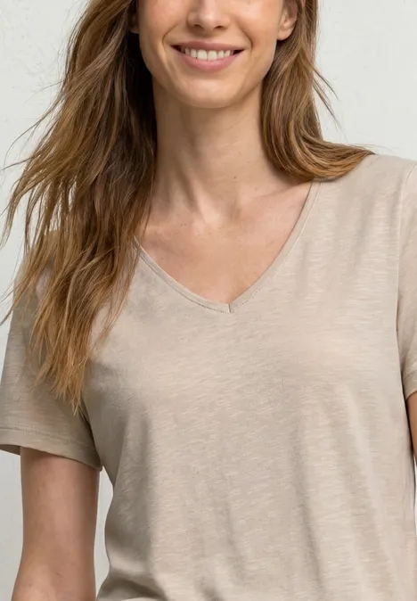 Basic shirt light sepia sand Eine lächelnde Frau in einem beigen, kurzärmeligen V-Ausschnitt-Oberteil, halbe Körperansicht.