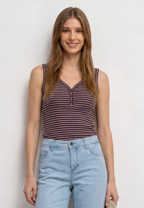 Top à col en V et à rayures rustic rouge Une femme posant devant un fond clair, vêtue d’un débardeur rayé et d’un jean clair.