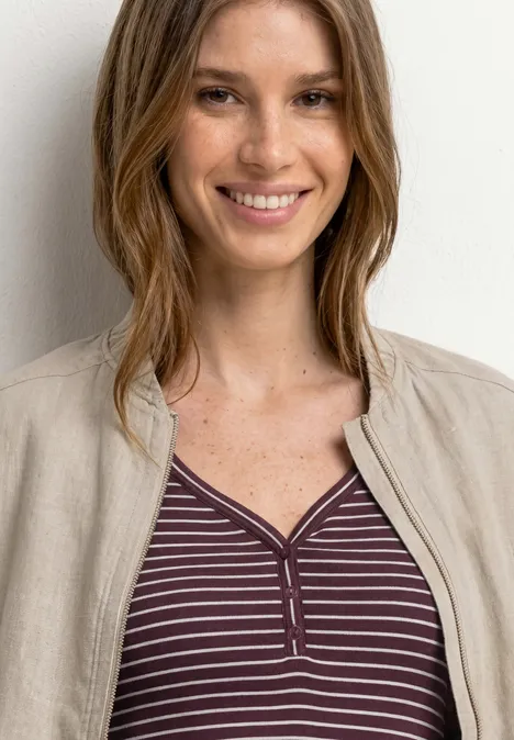 Top à col en V et à rayures rustic rouge Femme aux cheveux bruns porte un haut violet rayé et un blazer beige devant un mur clair.