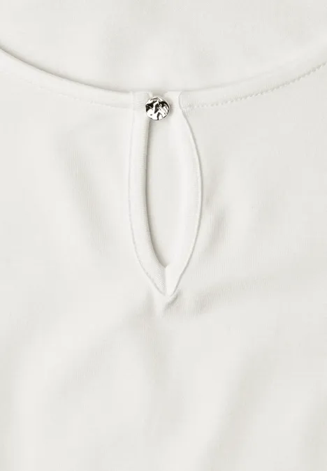 Haut blanc à encolure ronde, fente goutte d’eau et petit fermoir métallique.