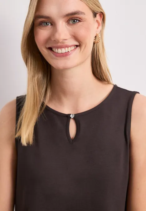 Une femme blonde porte un haut noir sans manches, avec une ouverture goutte et une boucle d'oreille dorée.