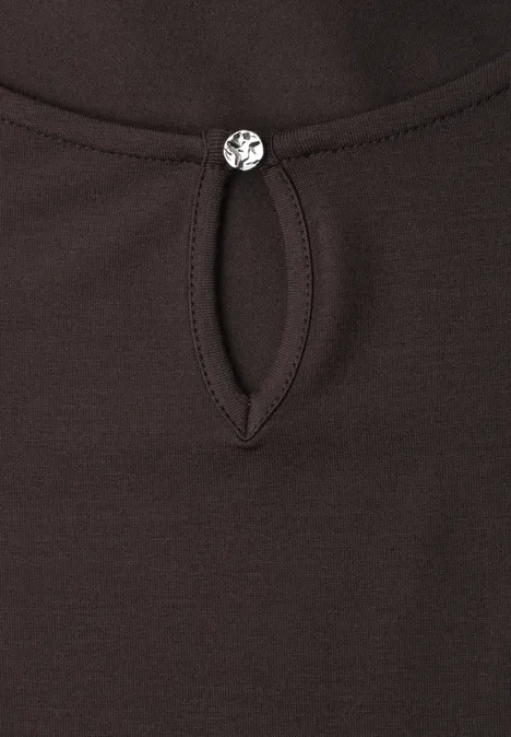 Gros plan d’un haut foncé avec une découpe en goutte au col, orné d’un petit bouton rond et scintillant.