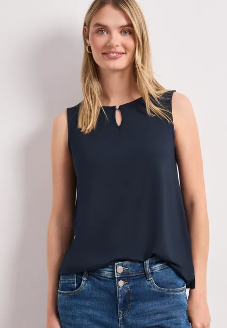 Femme porte un top sans manches bleu marine et un jean bleu.