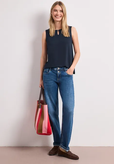Femme en débardeur marine, jeans bleus, mocassins marron et grand sac rayé rose et beige.