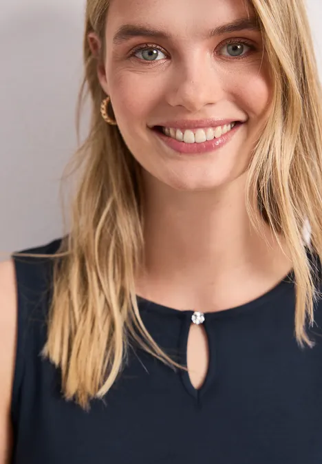 Femme blonde souriante en top bleu foncé avec encolure goutte d'eau et bouton décoratif