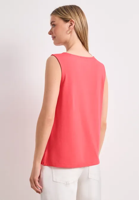 Vrouw van achteren in een koraalkleurige top en witte broek
