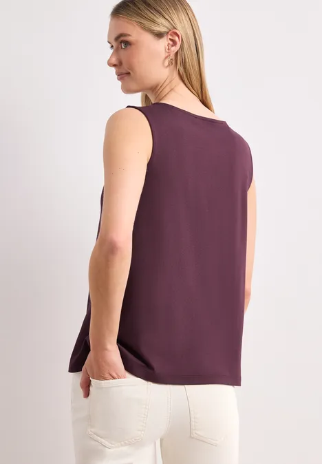 Femme vue de dos portant un haut sans manches bordeaux et un pantalon blanc.