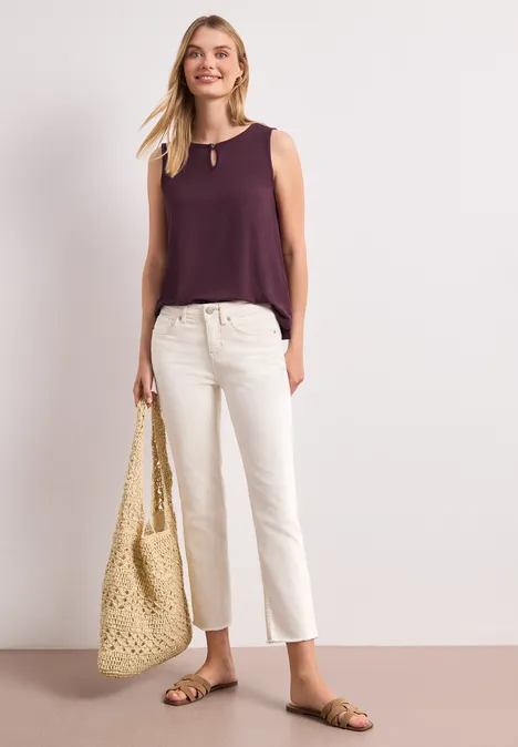 Femme en top violet, pantacourt blanc, sandales et grand sac de plage tressé.