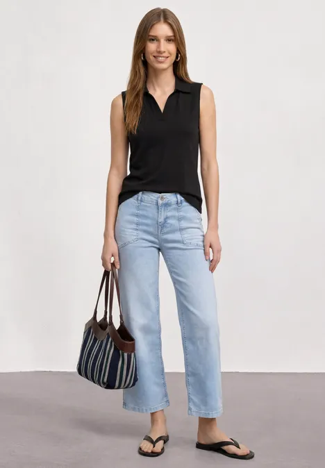 Vrouw in zwart topje, lichte jeans, zwarte slippers en gestreepte tas voor neutrale achtergrond.