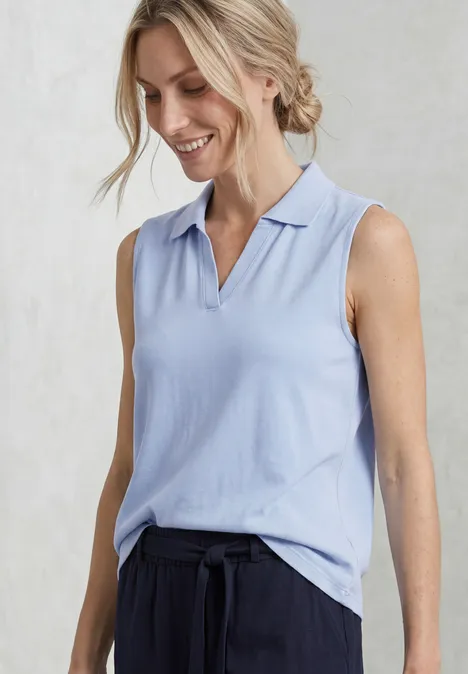 Top in Rippstruktur mit Polokragen cashmere blue Frau in ärmellosem hellblauem Polohemd und schwarzer Hose vor hellem Hintergrund.