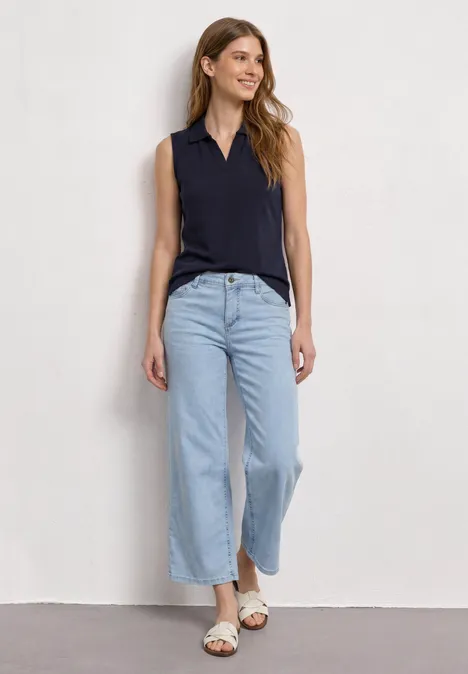 Femme en haut sans manches noir et jean large bleu clair avec sandales.