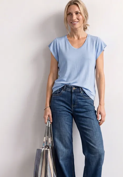 Frau trägt hellblaues T-Shirt, Jeans und hält eine transparente Tasche.