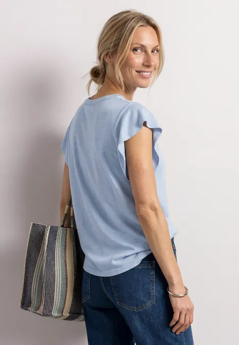 Frau in hellblauem Top und Jeans, trägt eine gestreifte Tasche über der Schulter.