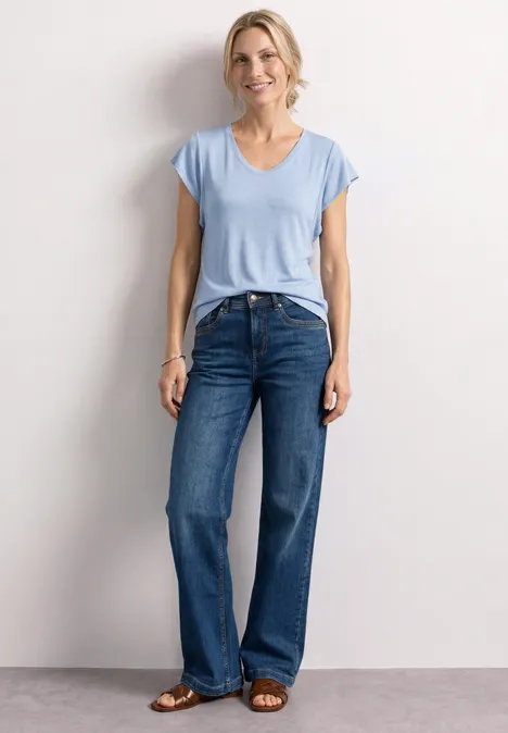 Frau trägt hellblaues T-Shirt und weite Jeans vor hellem Hintergrund