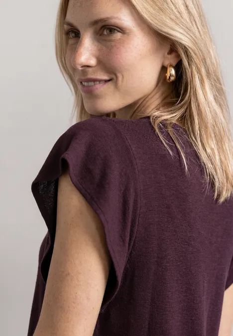Blonde Frau von hinten in ärmellosem violettem Top und goldenen Ohrringen.