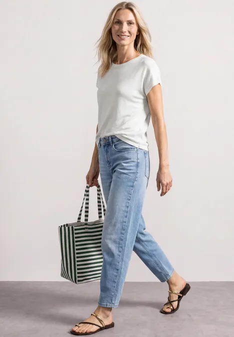 Dropped Shoulder Shirt mit Rundhals off white Frau in weißem T-Shirt, blauen Jeans und Sandalen trägt eine gestreifte Tasche und geht.