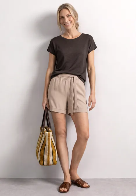 Dropped Shoulder Shirt mit Rundhals espresso brown Frau trägt schwarzes T-Shirt, beige Shorts und braune Sandalen, hält eine gelb-weiße gestreifte Tasche.