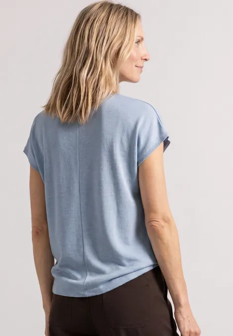 Dropped Shoulder Shirt mit Rundhals cashmere blue Eine Frau von hinten in einem hellblauen T-Shirt und dunklen Hosen, stehend und seitlich blickend.
