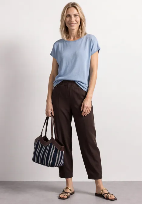 Dropped Shoulder Shirt mit Rundhals cashmere blue Frau trägt hellblaues T-Shirt, braune Hose, Sandalen und hält eine gestreifte Tasche.