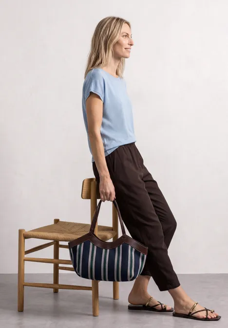 Dropped Shoulder Shirt mit Rundhals cashmere blue Seitlich stehende Person in lässiger Kleidung lehnt am Stuhl und hält eine gestreifte Tasche.