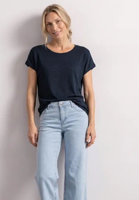Dropped Shoulder Shirt mit Rundhals shadowed navy Eine Person trägt ein schwarzes T-Shirt und hellblaue Jeans vor einem hellen Hintergrund.