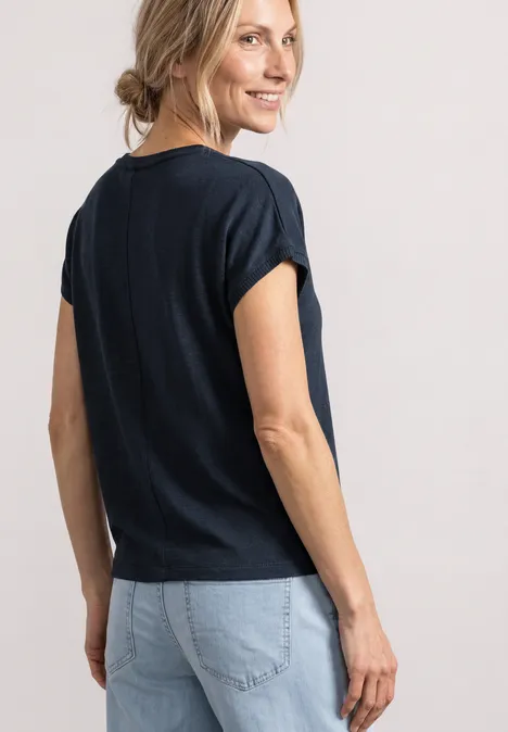 Dropped Shoulder Shirt mit Rundhals shadowed navy Eine Frau im Profil dreht sich lächelnd um, trägt dunkelblaues T-Shirt und helle Jeans.