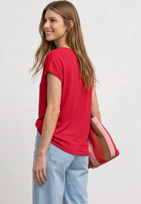 Vrouw in rood T-shirt en blauwe spijkerbroek, zijwaarts, met een gestreepte tas.