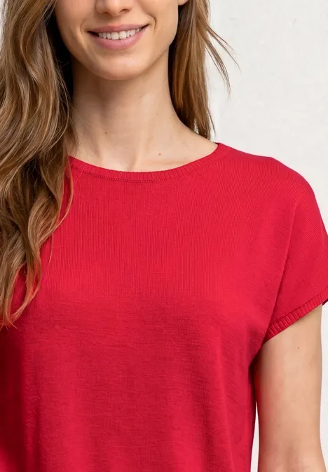 Vrouw lacht in rood T-shirt met korte mouwen, alleen bovenlichaam zichtbaar.