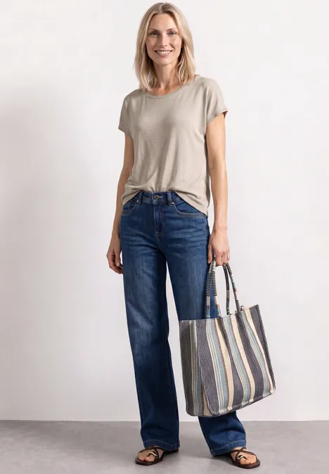 Vrouw in beige T-shirt, blauwe jeans en zwarte schoenen met gestreepte shopper.
