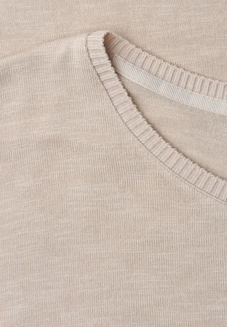 Close-up van de halslijn van een beige gebreide trui.