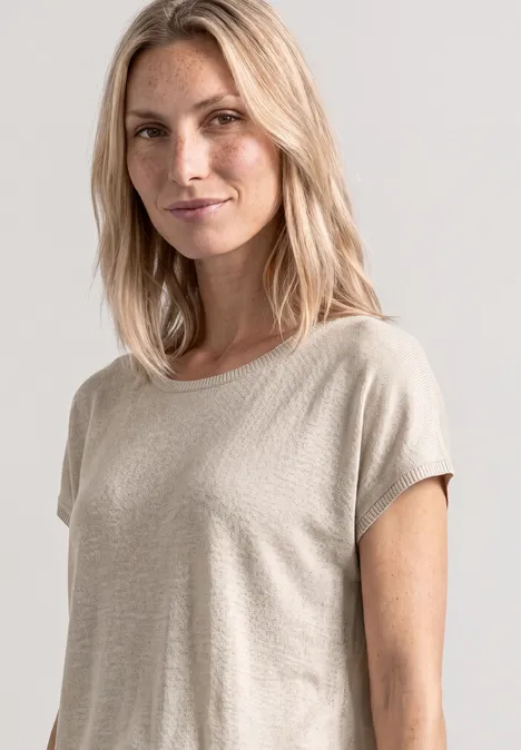 Vrouw in beige T-shirt met halflang blond haar voor een neutrale lichtgrijze achtergrond.