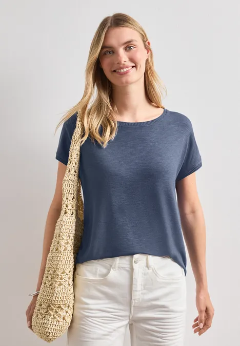 Dropped Shoulder Shirt mit Rundhals ashen blue Frau in blauem T-Shirt und weißer Hose mit Basttasche über der Schulter.