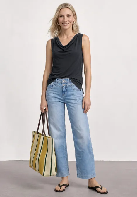 Silk-Look Top mit Wasserfall-Ausschnitt Black Frau trägt schwarzes ärmelloses Top, helle Jeans mit weitem Bein, schwarze Flip-Flops und gestreifte Tragetasche.