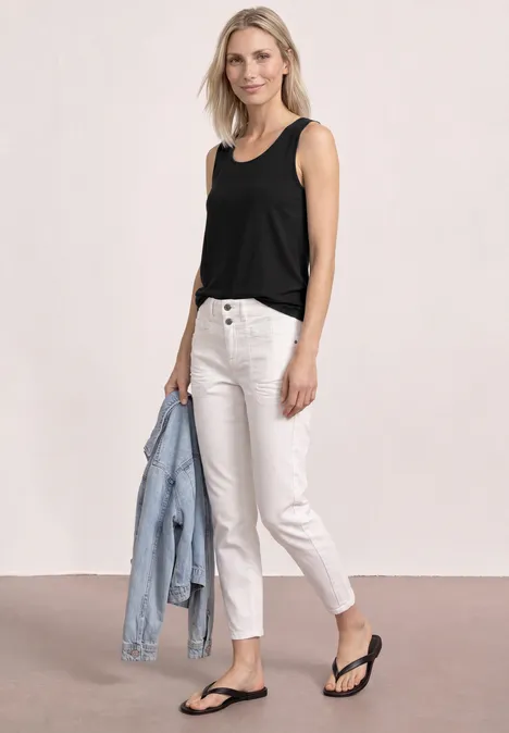 Eine Frau trägt ein schwarzes Top, weiße Jeans, schwarze Flip-Flops und hält eine hellblaue Jeansjacke.