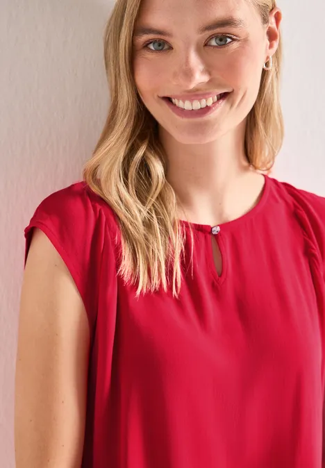 Jonge vrouw met lang blond haar draagt een rood shirt en glimlacht vriendelijk.