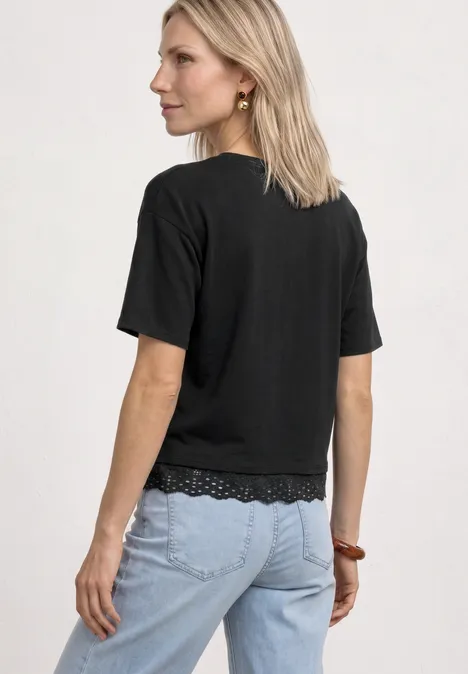 Frau von hinten mit schulterlangem blondem Haar, schwarzem T-Shirt mit Spitze und hellblauer Jeans