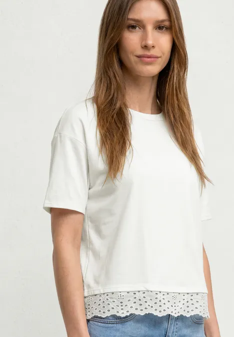 Frau trägt ein weißes T-Shirt mit kurzen Ärmeln und verspieltem Spitzenbesatz am Saum.