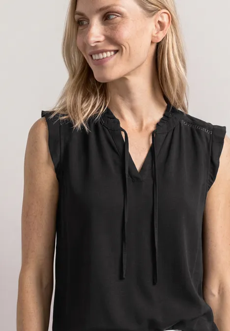 Blonde vrouw in zwarte mouwloze top lacht zachtjes opzij.