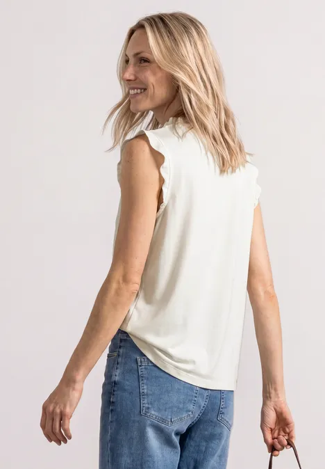 Vrouw van achteren gezien met blond haar, draagt een mouwloos wit topje, spijkerbroek en houdt een donkere clutch.