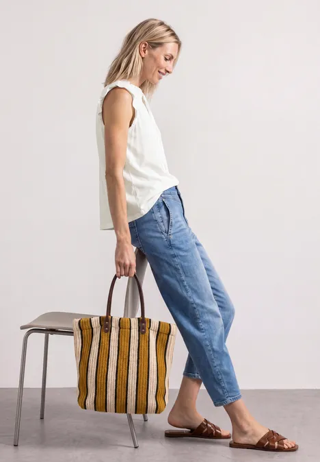 Vrouw met wit topje, blauwe jeans en bruine sandalen, draagt een gestreepte tas.